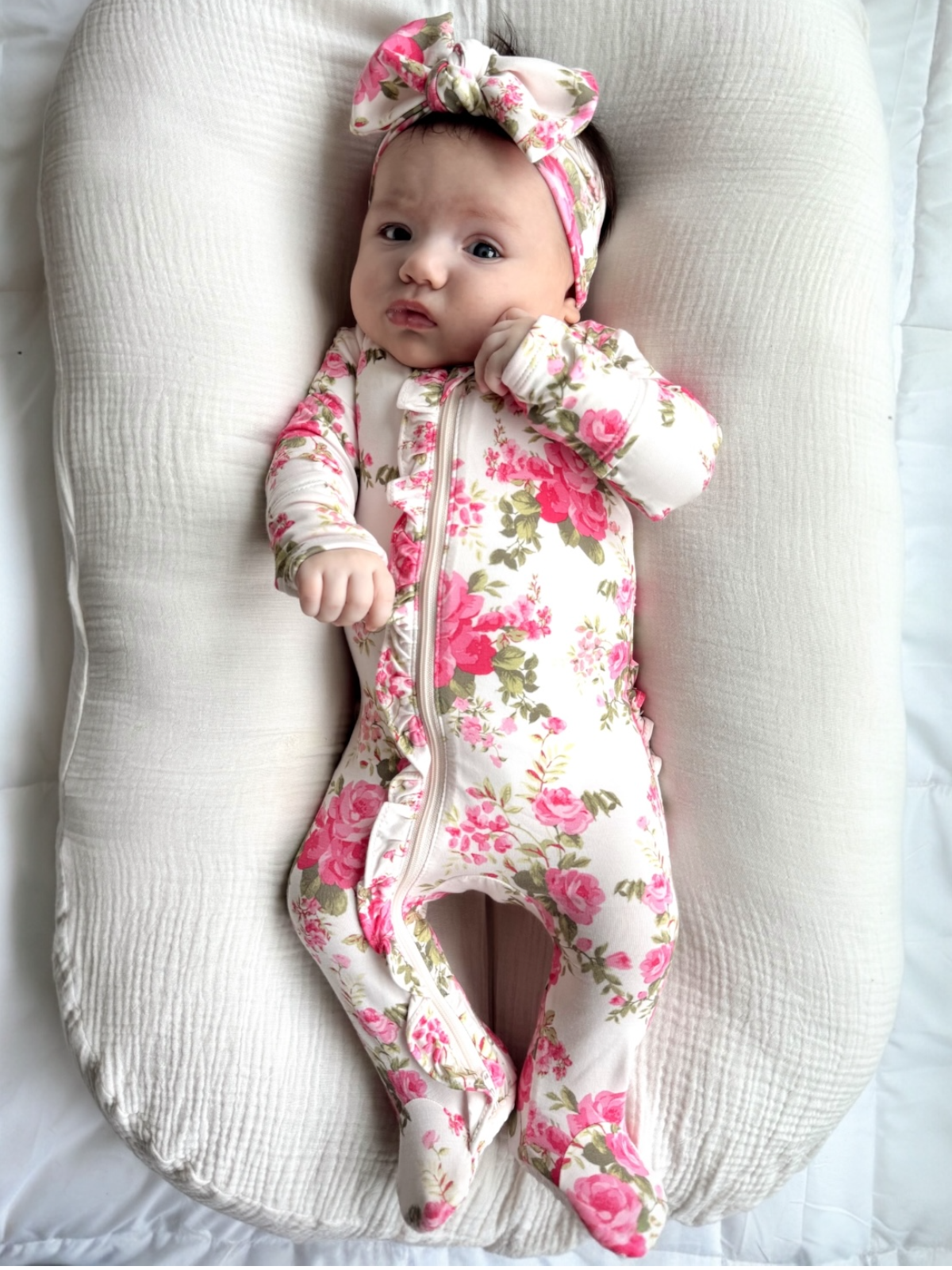 Baby in a floral onesie and headband lying on a textured surface
