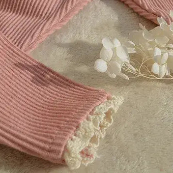 Pink ribbed fabric with lace trim on a beige surface with white flowers.