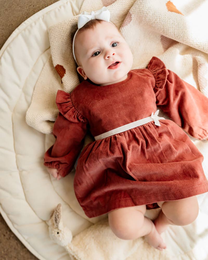 Baby in a rust-colored dress lying on a soft surface