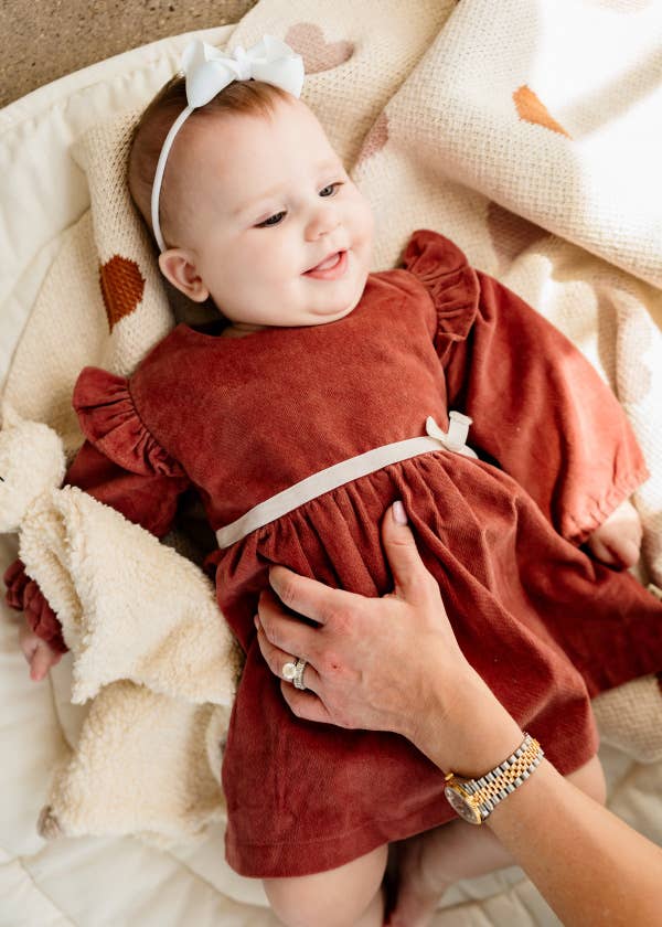 Baby in a rust-colored dress with a white bow lying on a soft surface