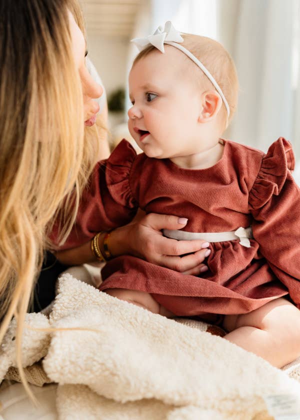Woman holding a baby wearing a rust-colored dress with ruffles.
