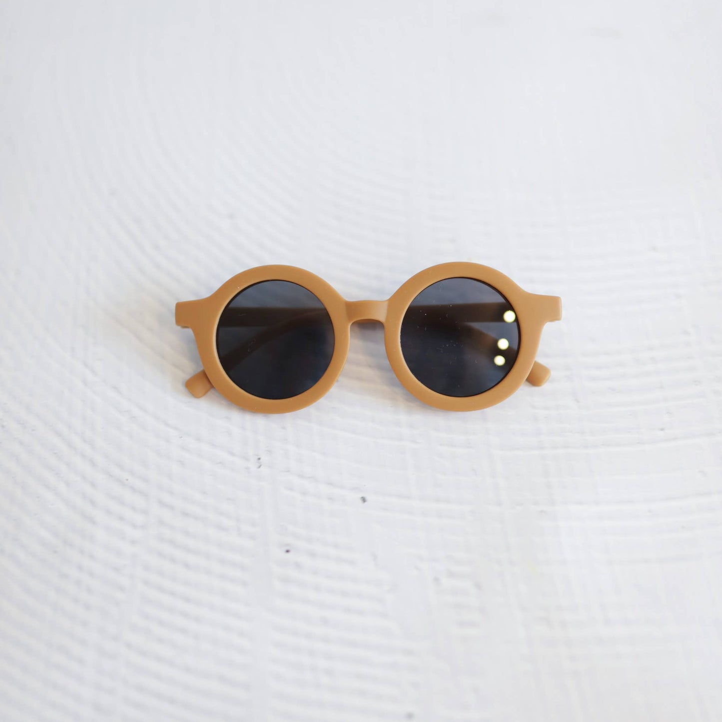 Round sunglasses with brown frame and dark lenses on a white textured background