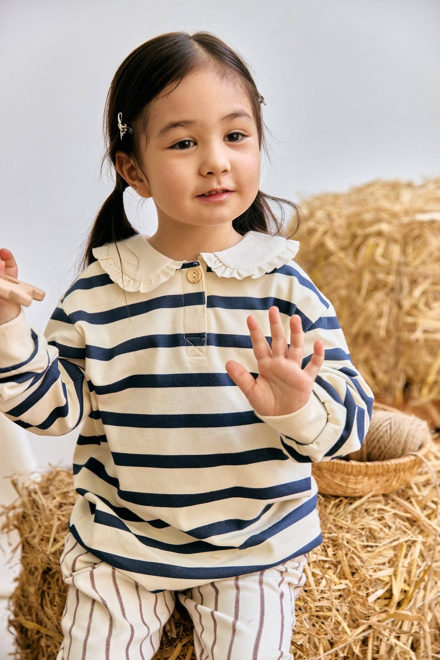 Child wearing a striped shirt and pants sitting on hay bales.