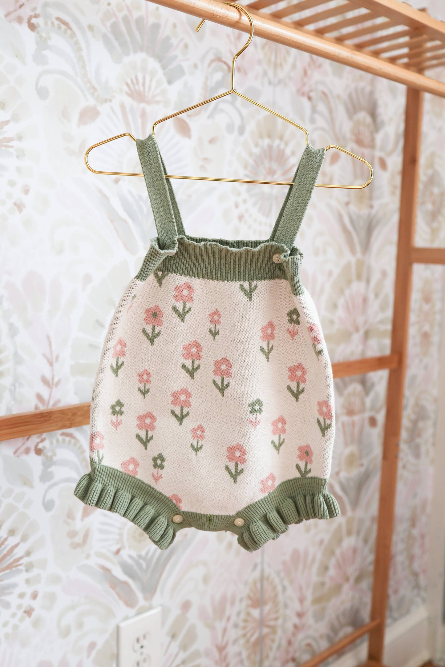 Children's floral dress with green straps and ruffles hanging on a rack.