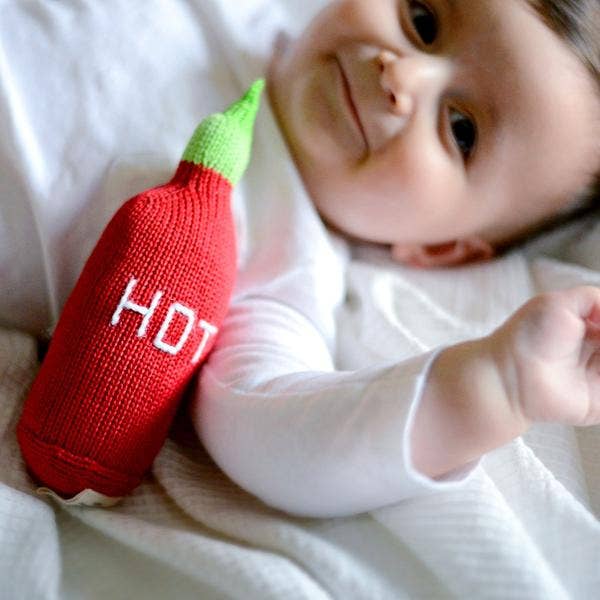 Baby holding a red knitted chili pepper toy with 'HOT' text.