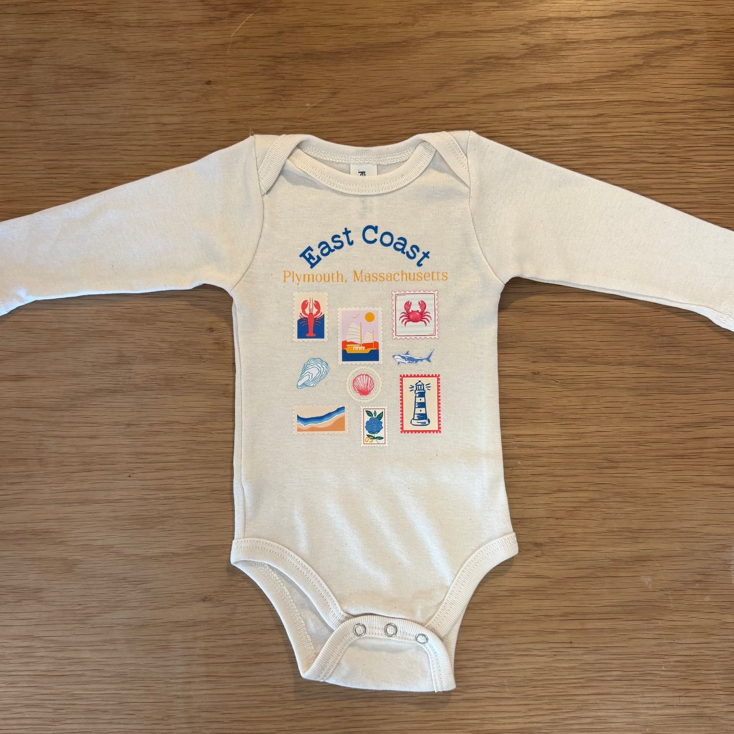 Ivory onesie with East Coast Plymouth Massachusetts printed on it. Nautical prints on the shirt as well such as lobsters, sharks, oysters, seashells, sail boats, the beach, and hydrangeas.