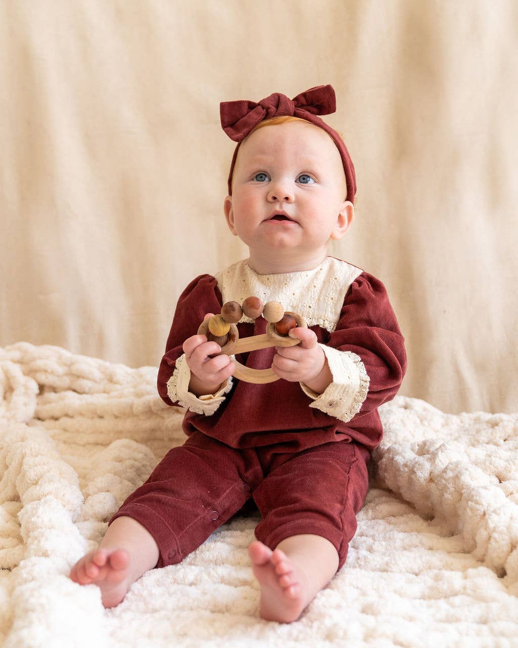 Baby in a red outfit with a bow, sitting on a soft surface