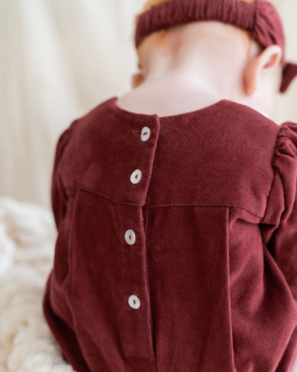Child wearing a burgundy dress with buttons and matching headband on a soft white background