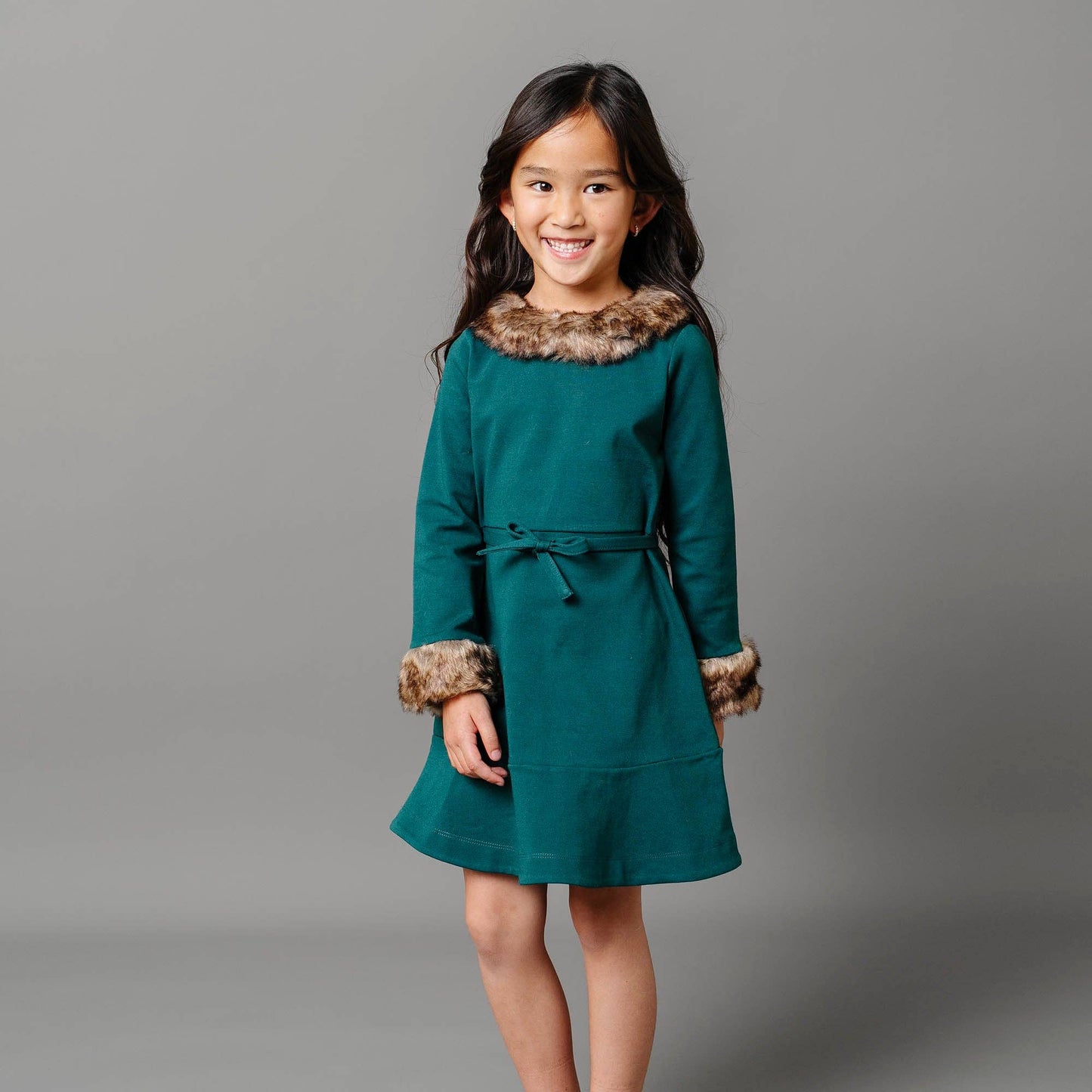 Young girl wearing a teal dress with fur trim against a gray background