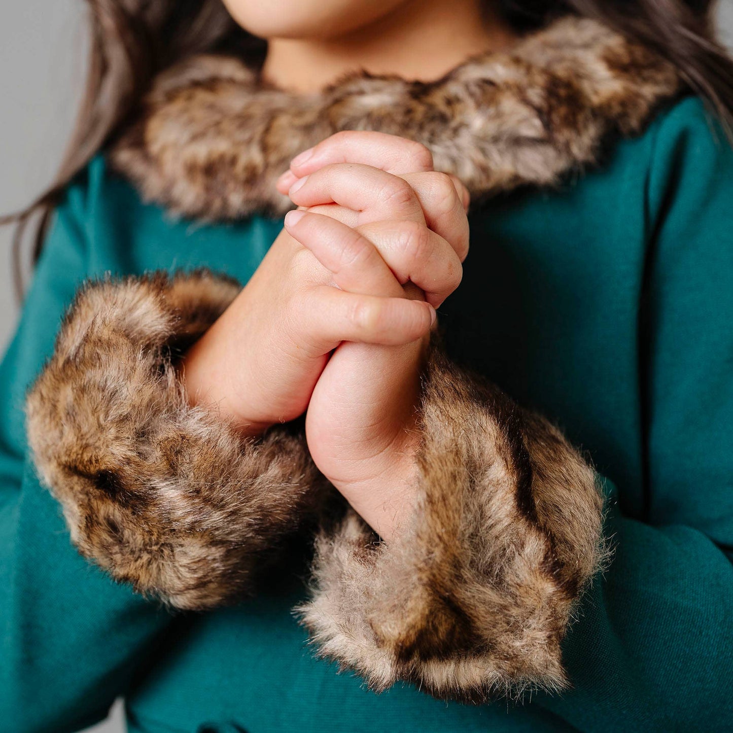 Close-up of hands wearing fur-trimmed gloves with a teal coat and fur collar.
