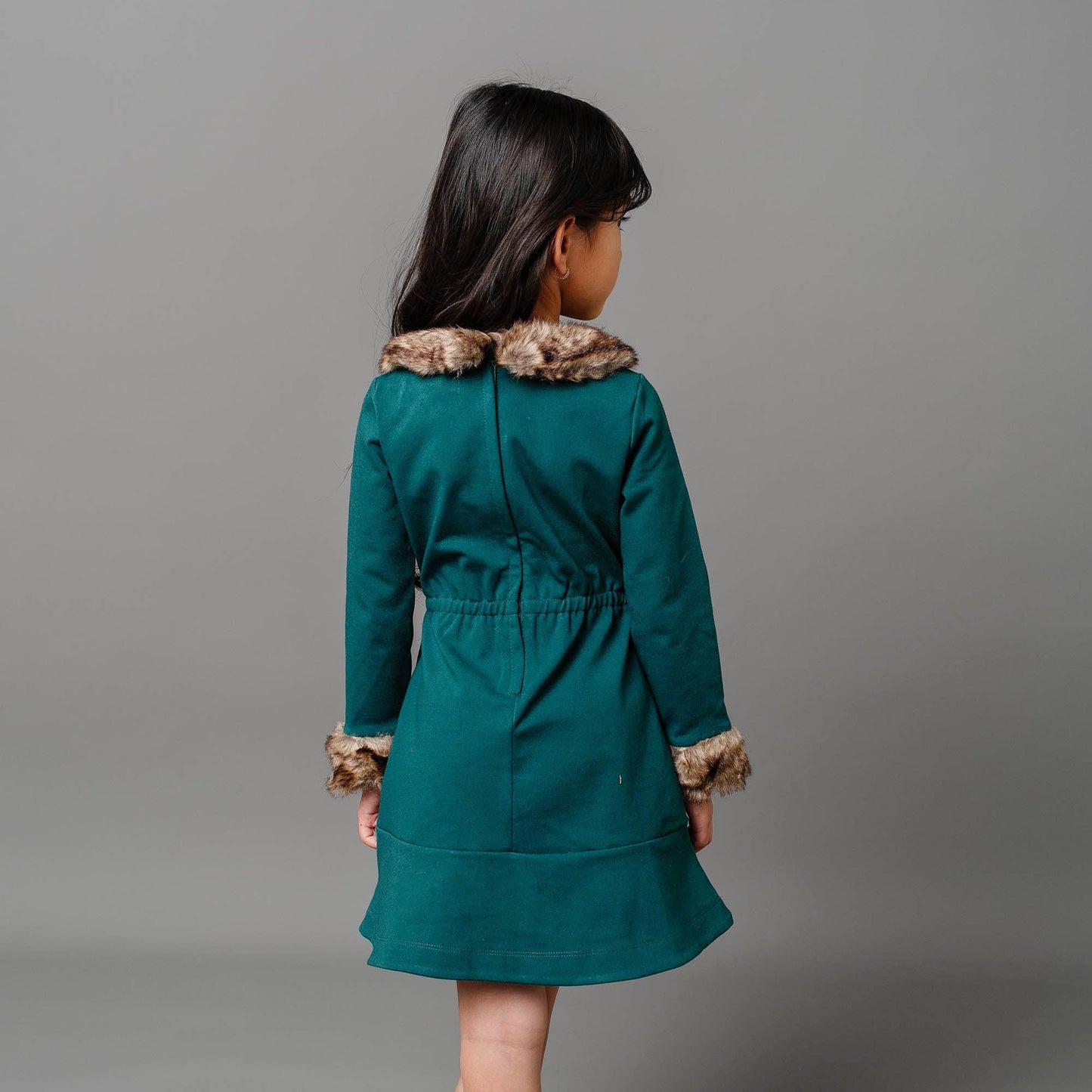 Child wearing a teal coat with fur trim on a gray background