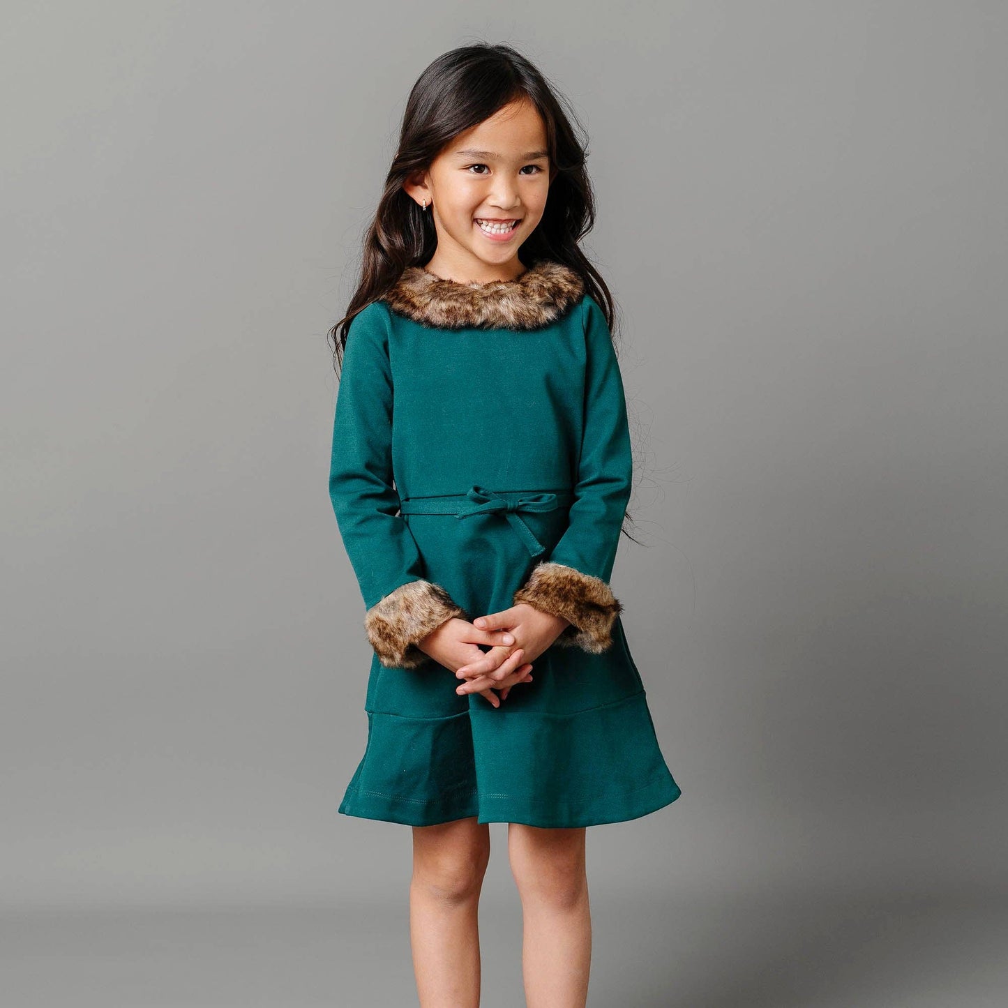 Young girl wearing a teal dress with fur trim on a gray background