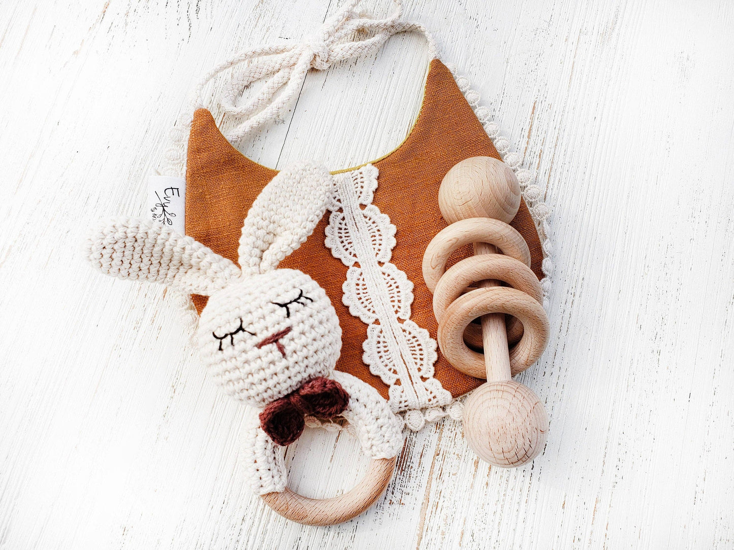 Baby bib with crochet bunny and wooden rattle on a white background