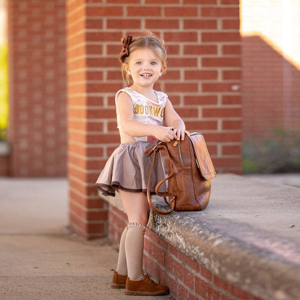 Young girl with a brown backpack standing against a brick wall.
