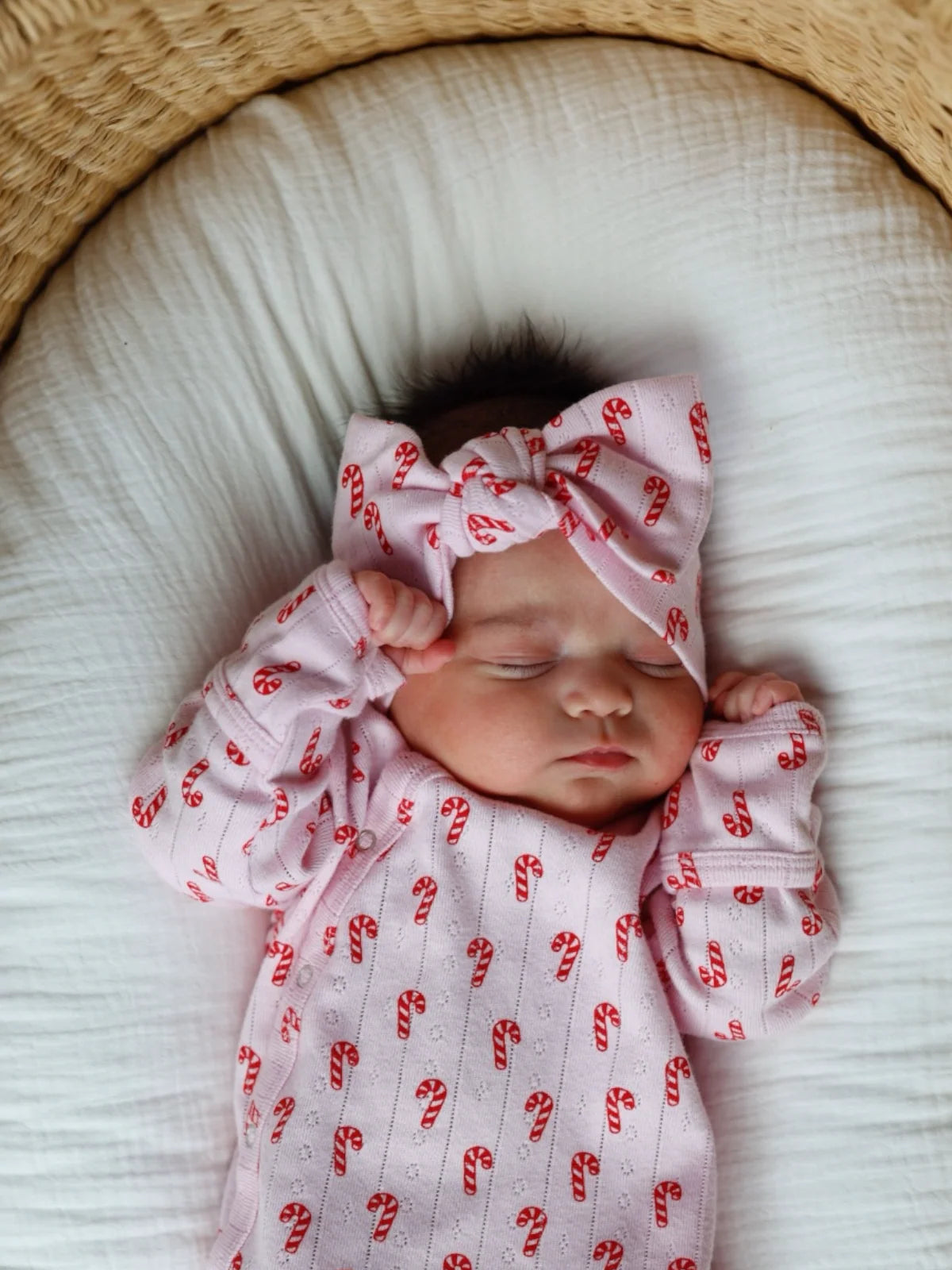 Newborn baby wearing a pink outfit with candy cane pattern and matching headband.