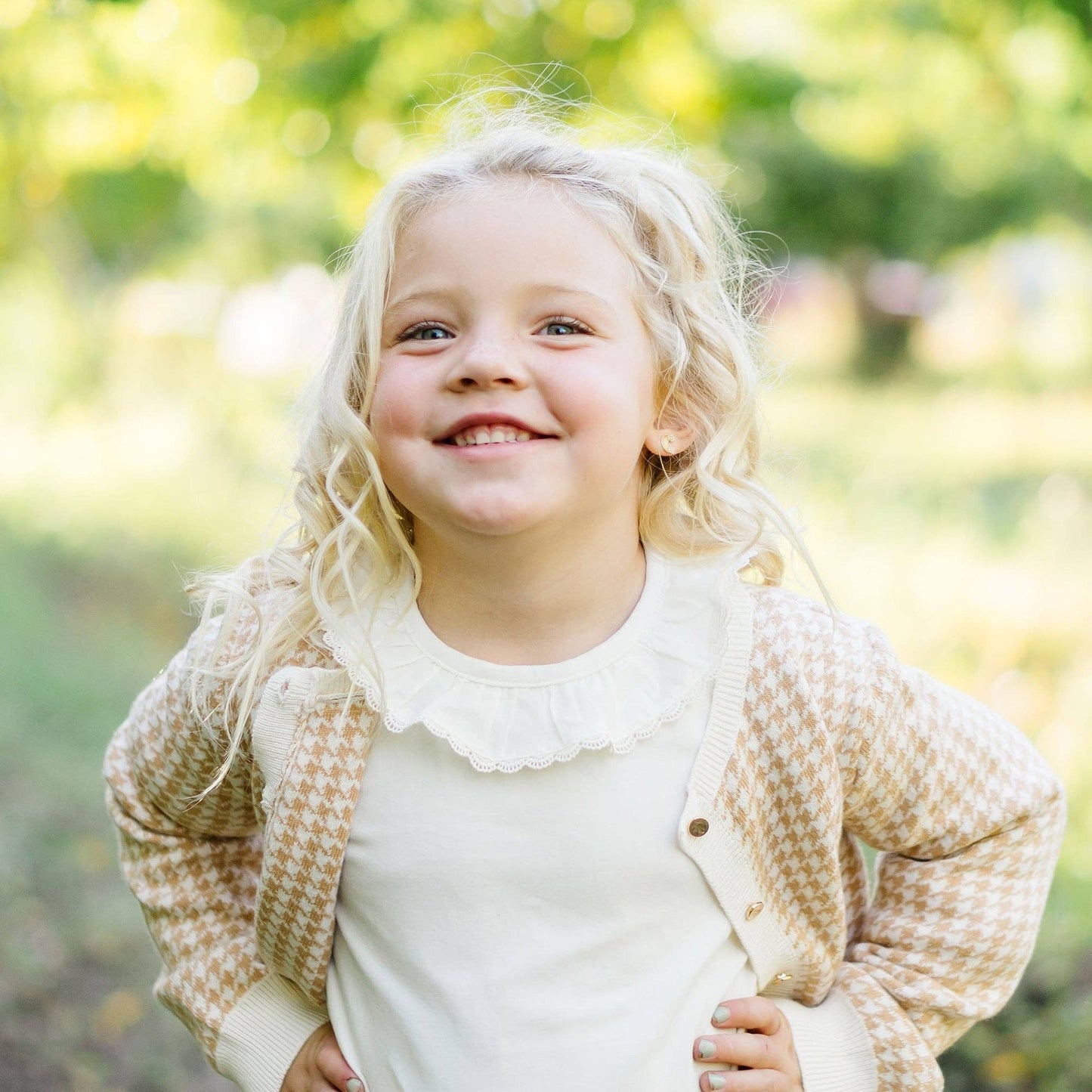 Young girl with blonde hair wearing a beige cardigan in a park setting