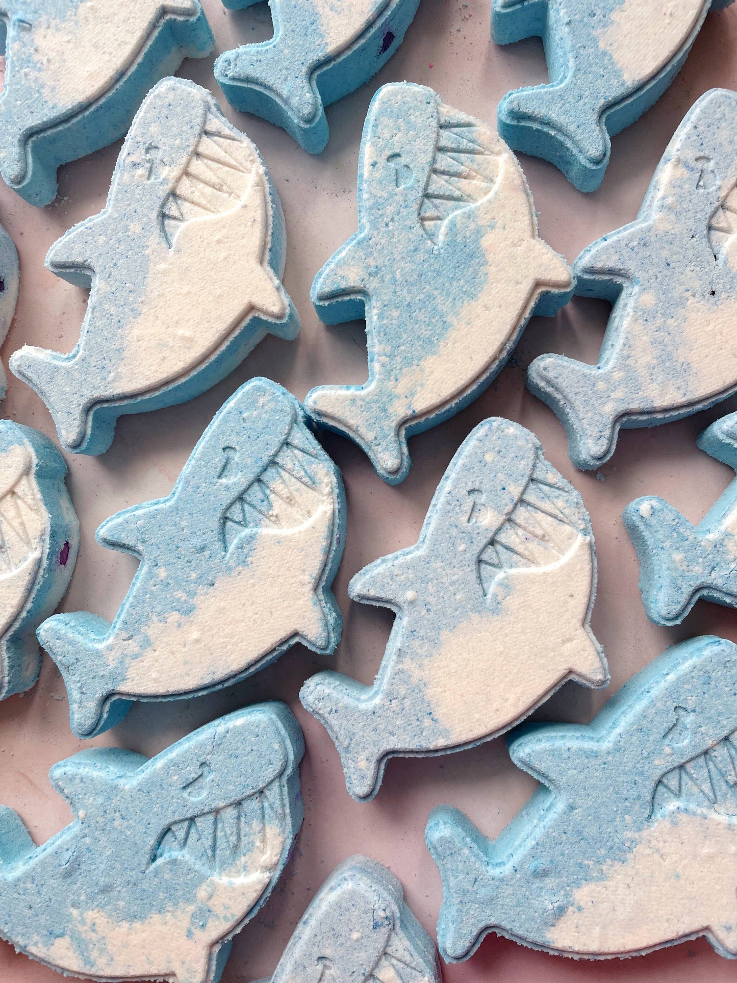 Collection of shark-shaped bath bombs with glittery texture on a pink background