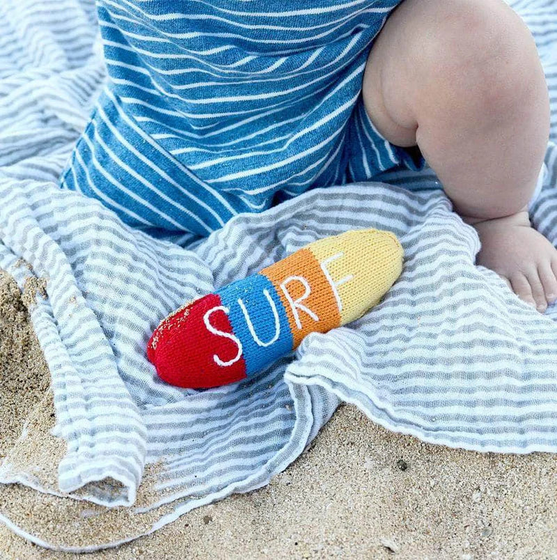 Colorful 'SURF' beach toy on a striped towel with a child's legs in the background.
