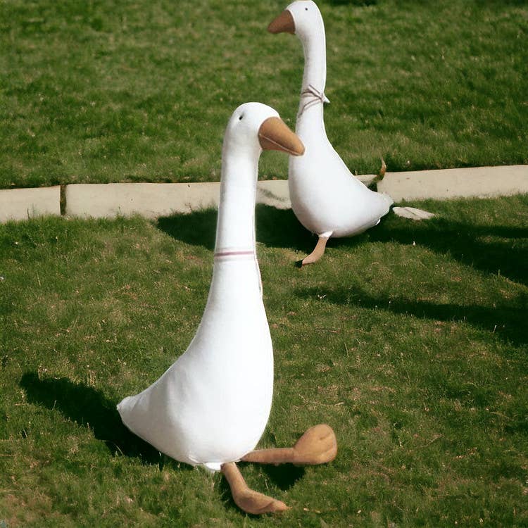 Two large white goose decoys on a grassy field.