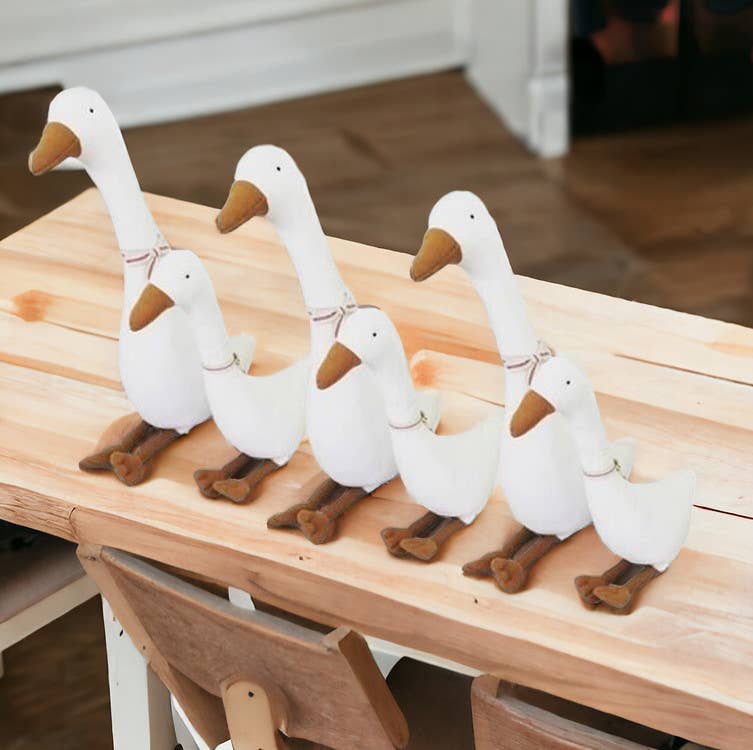 Five white goose figurines with brown feet and beaks on a wooden surface.