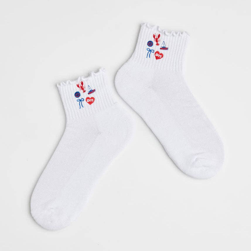 A pair of white ankle socks with a ruffled edge and small colorful embroidered cartoon motifs near the cuff, displayed on a light gray background.