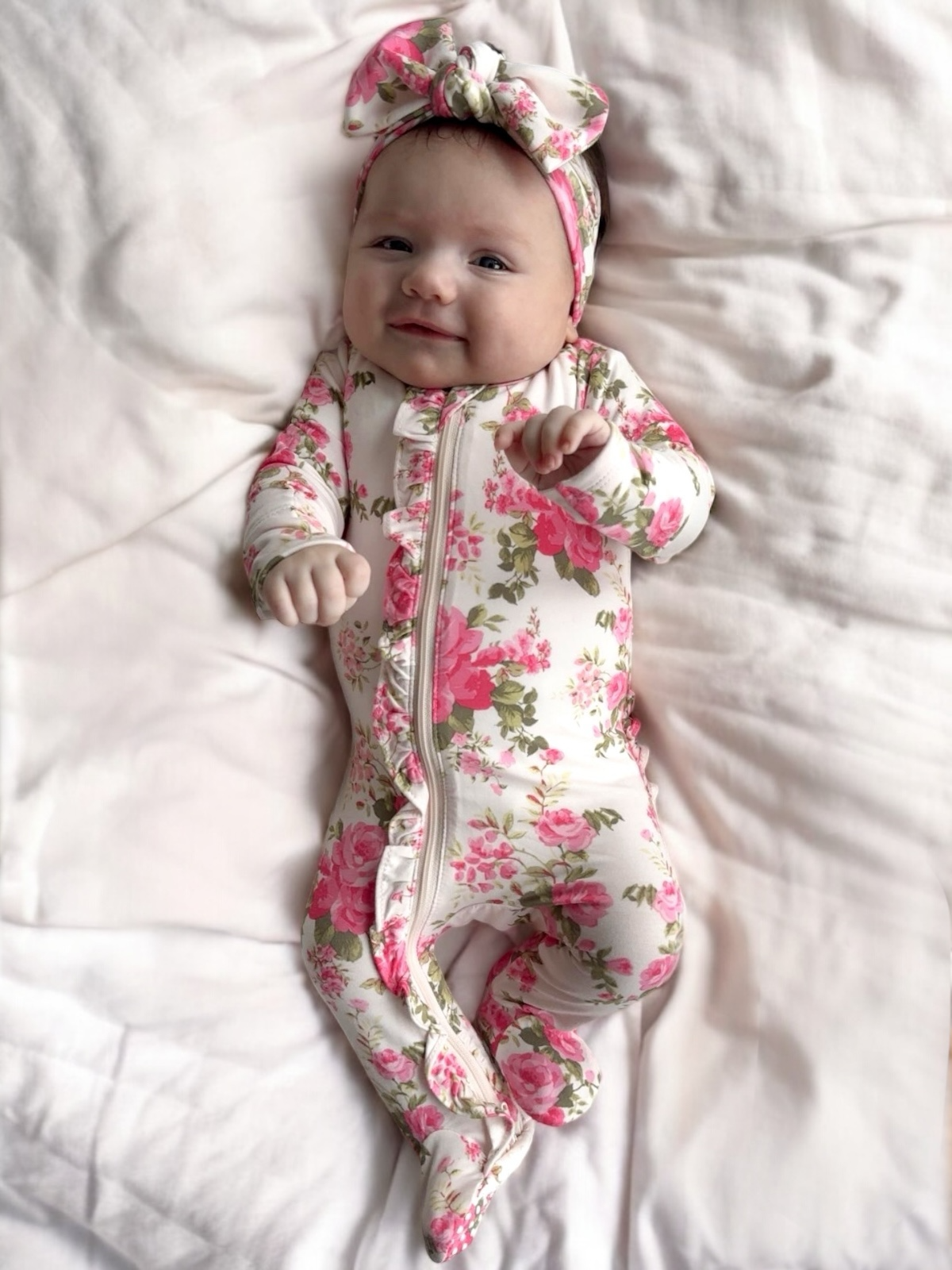Baby in a floral onesie and headband lying on a white blanket