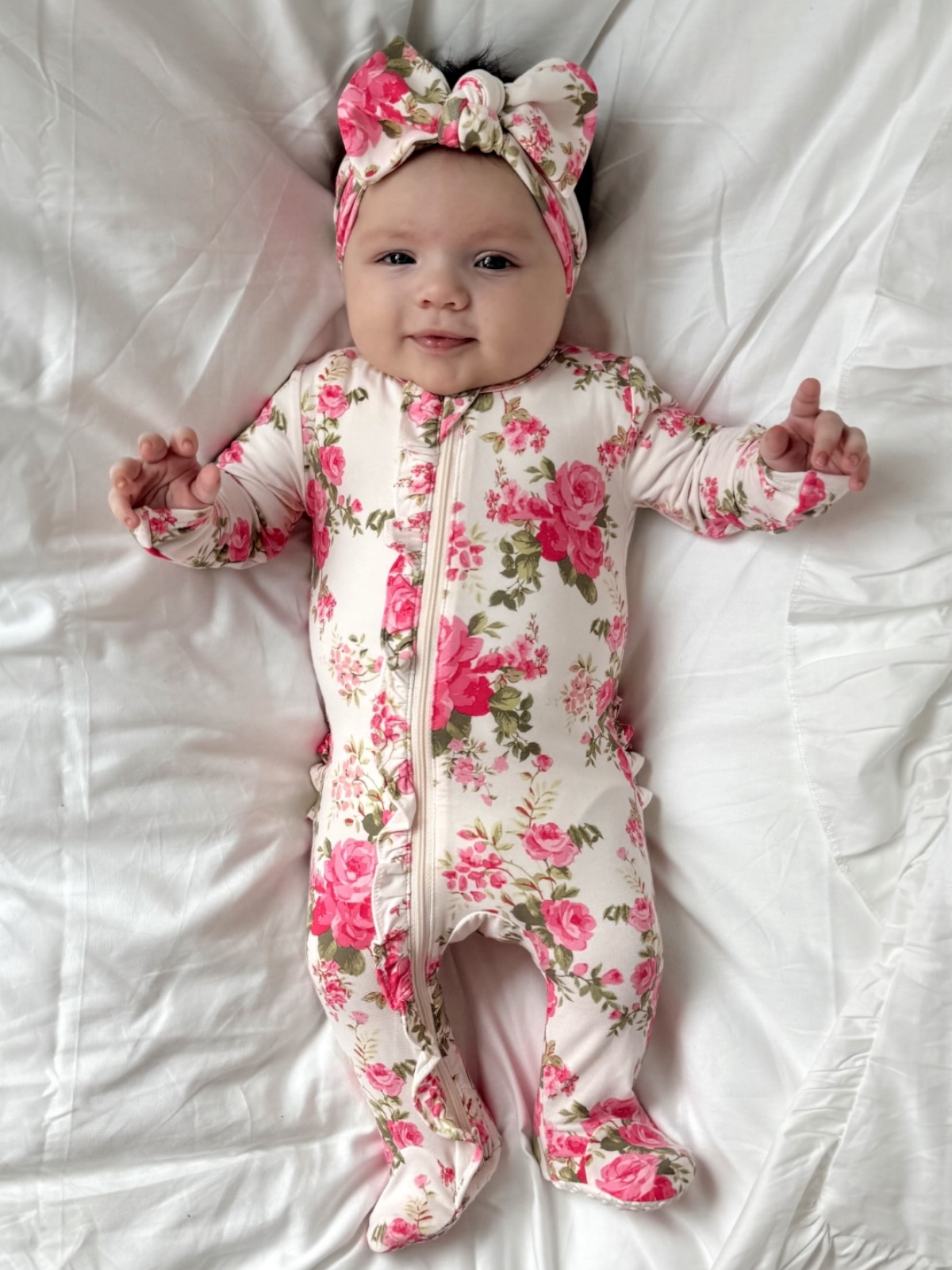 Baby wearing a floral onesie and headband lying on a white blanket
