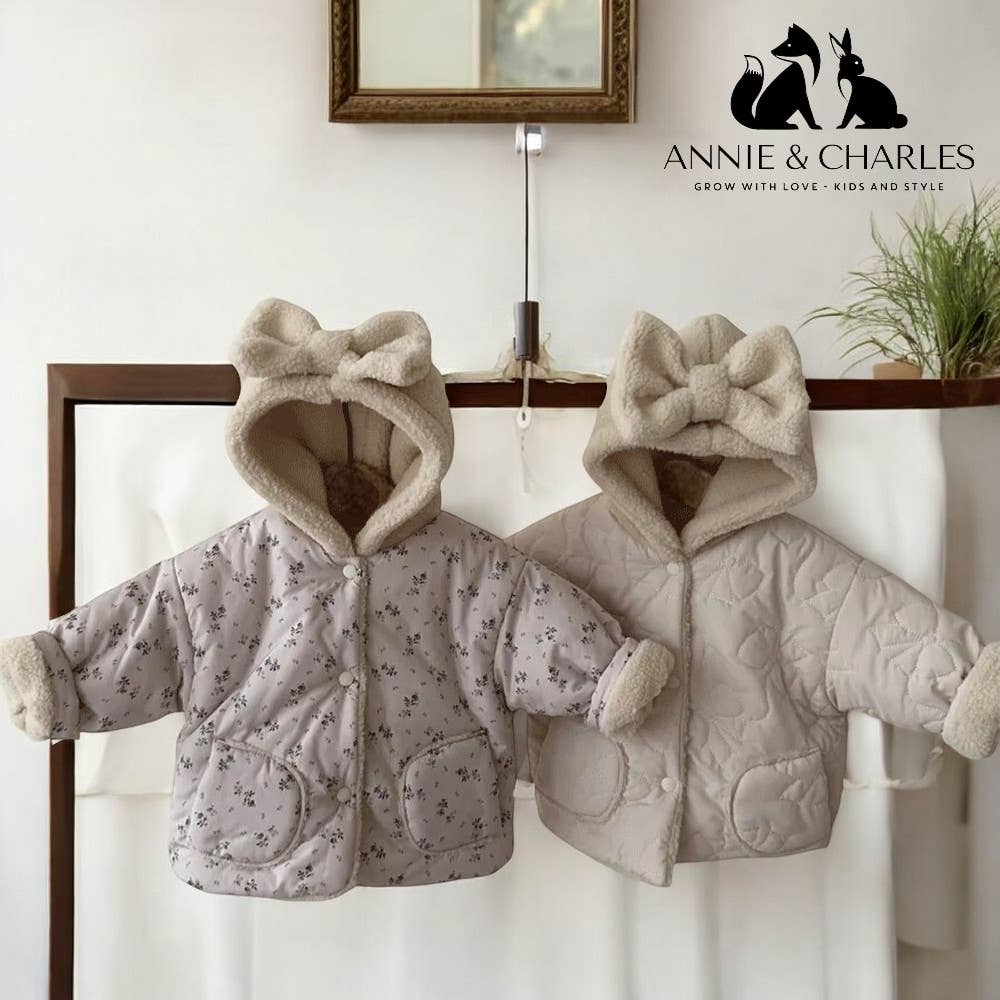 Two children's jackets with bow details hanging on a rack, branded 'Annie & Charles'.
