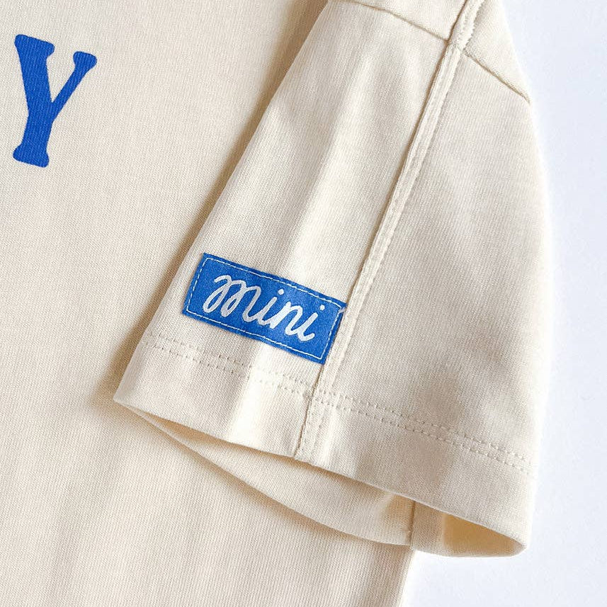 Beige shirt with blue patch that reads "mini" on a white background