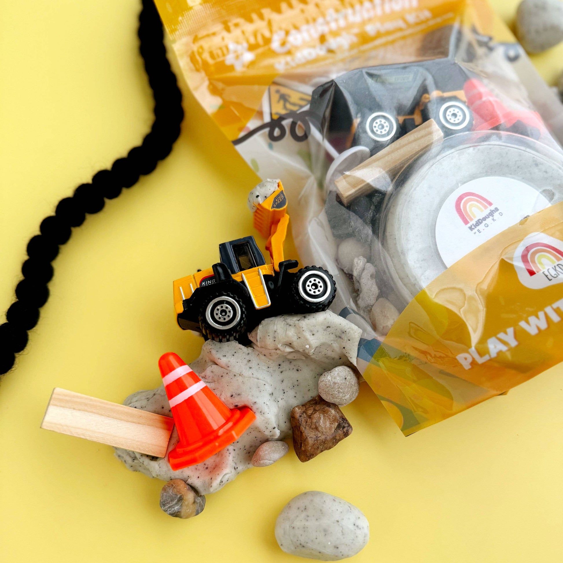 Construction-themed playset with toys and rocks on a yellow background