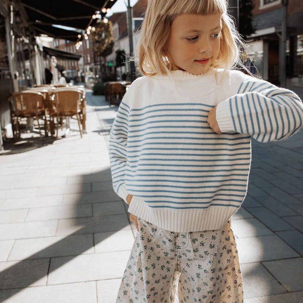 Child wearing a striped sweater and patterned pants on a city street.