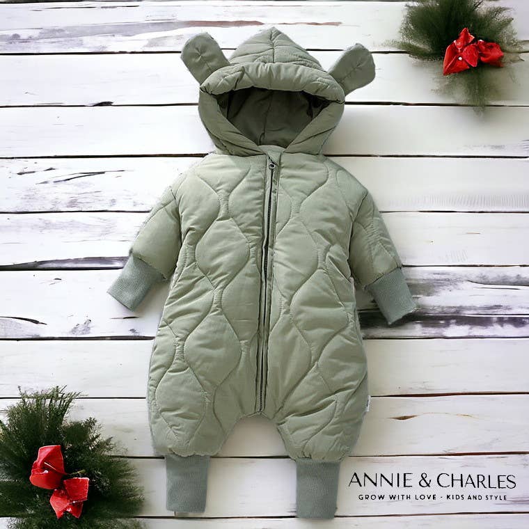 Green baby snowsuit with bear ears on a wooden surface, branded 'Annie & Charles'.