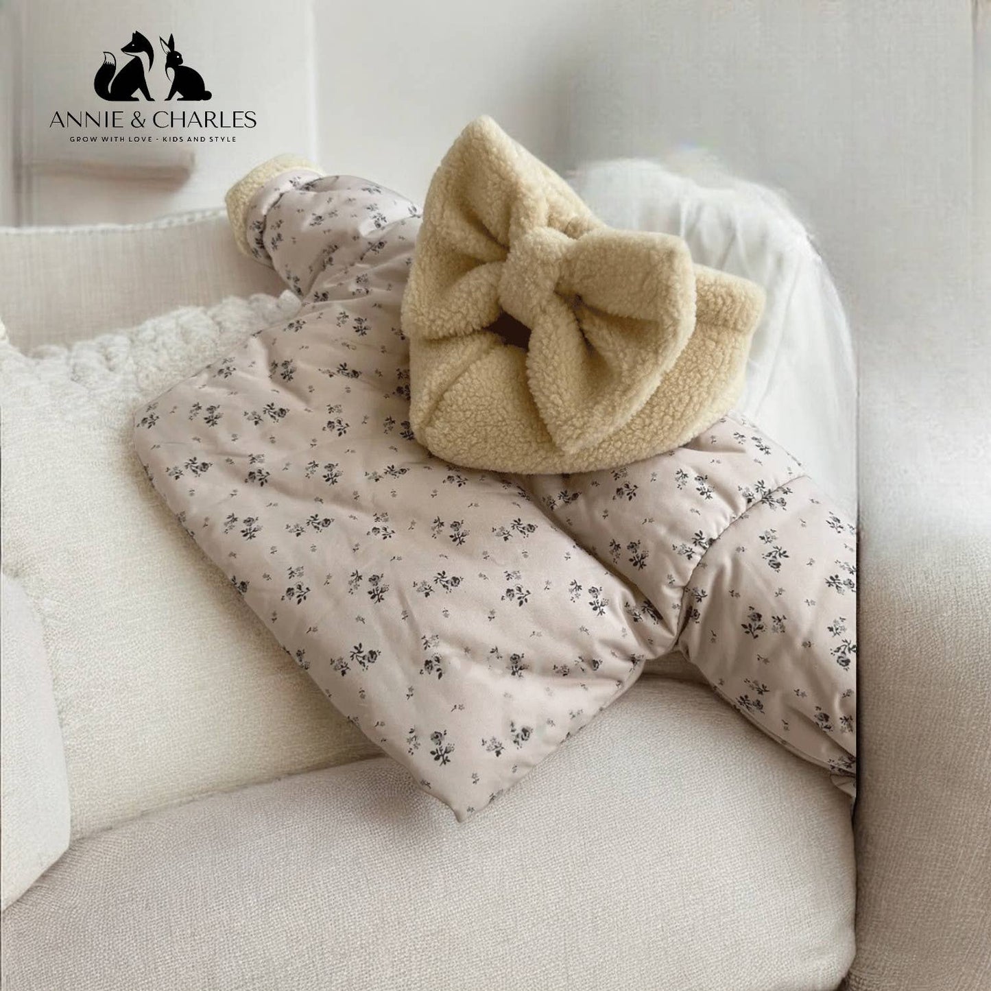 Floral-patterned baby blanket with a beige bow on a white couch, featuring the Annie & Charles brand.