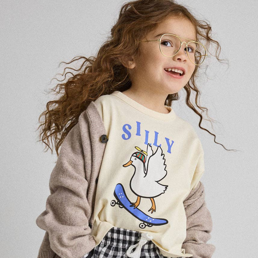 Child wearing a 'Silly' graphic sweatshirt with a duck on a skateboard and checkered shorts.