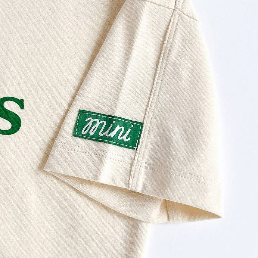 Beige shirt with a green label that says "mini" on a white background