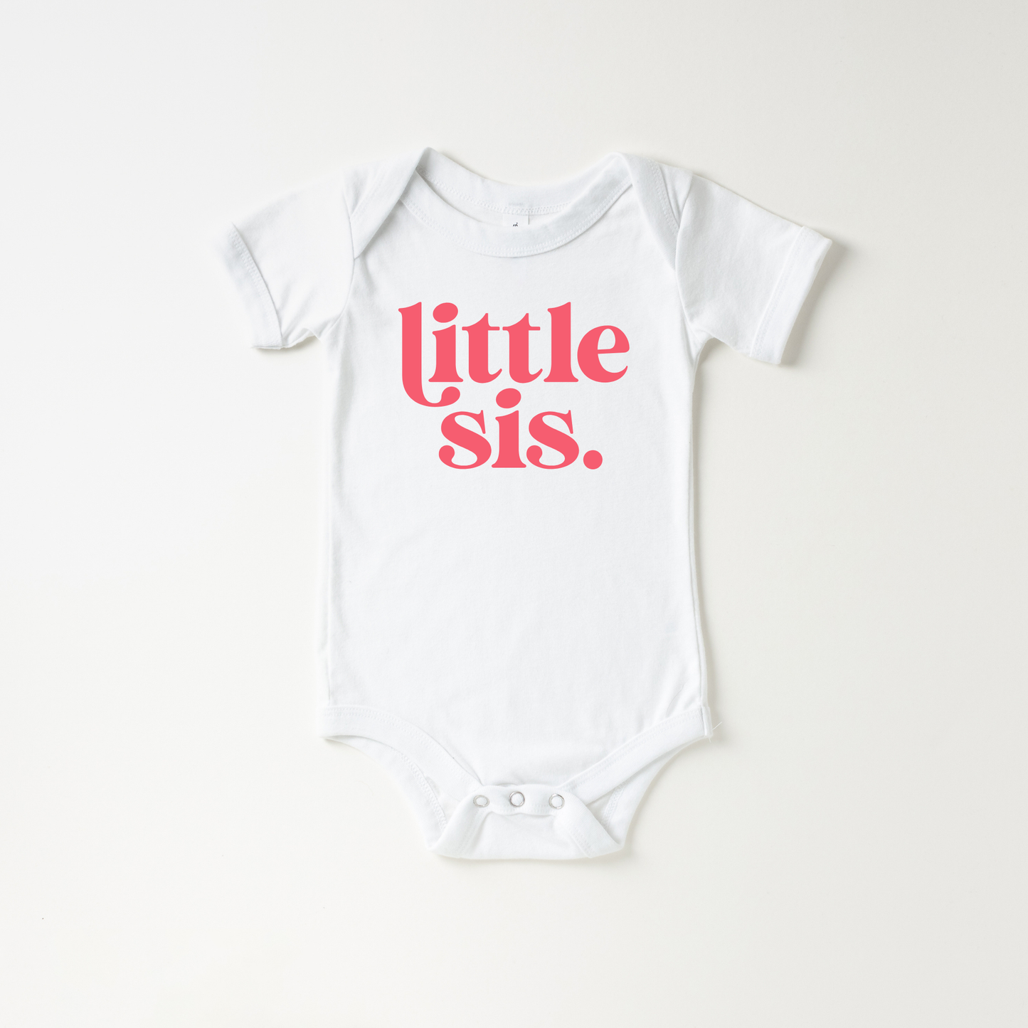 White baby onesie with 'little sis' text in pink on a white background