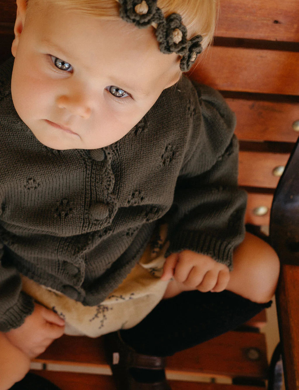 Child wearing a dark sweater and headband sitting on a wooden bench.