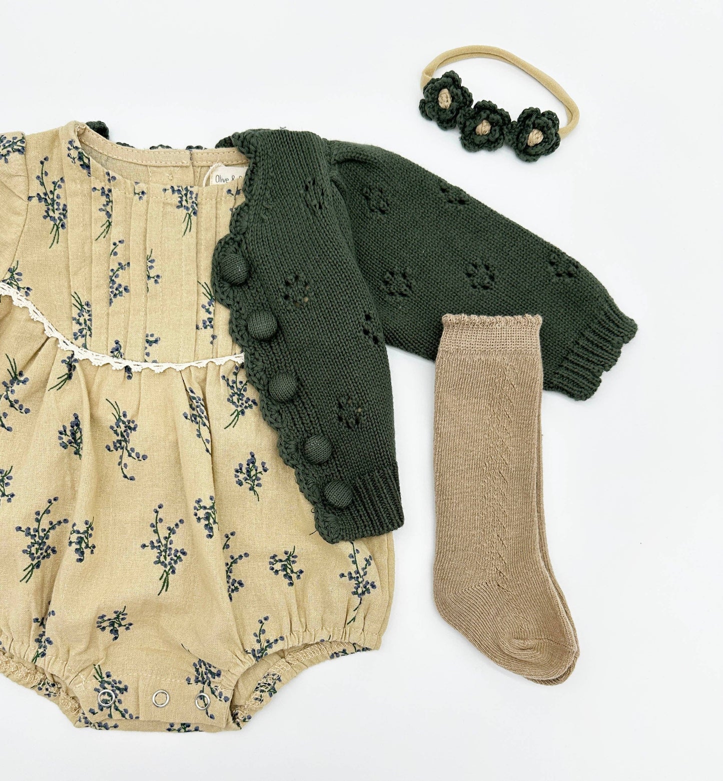 Baby outfit with floral romper, green cardigan, beige socks, and headband on a white background