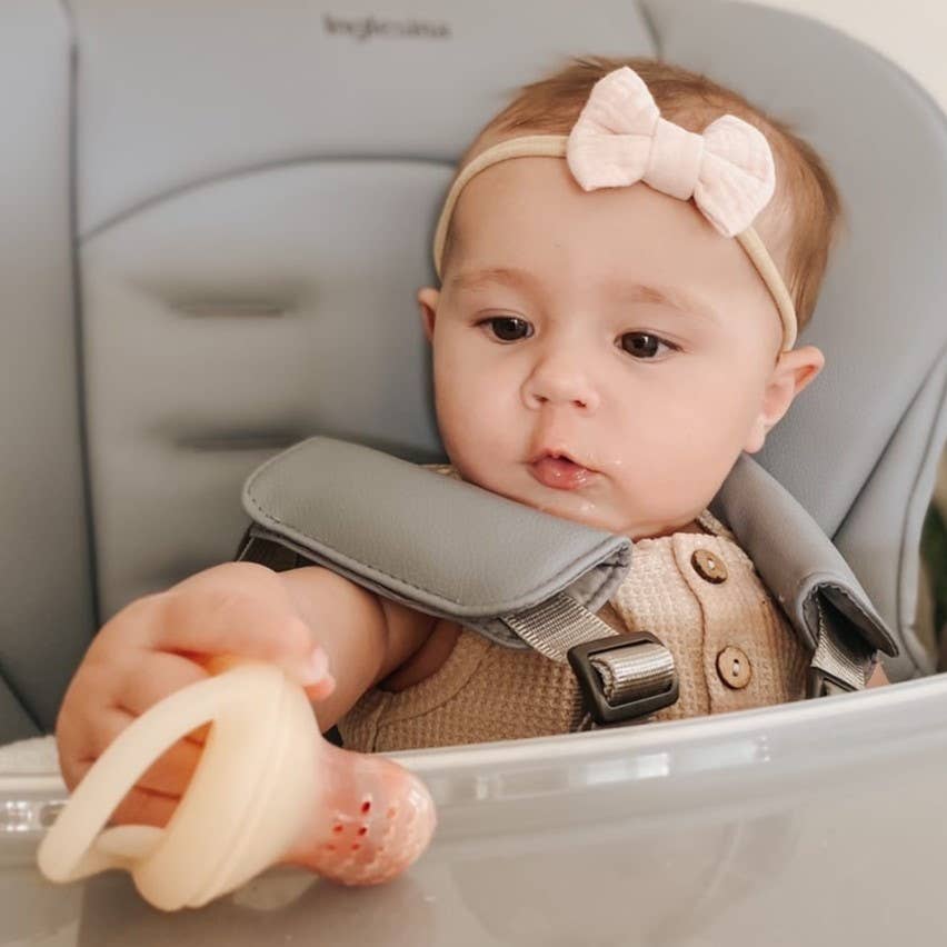 Baby in a high chair wearing a bow headband and holding a teething ring.