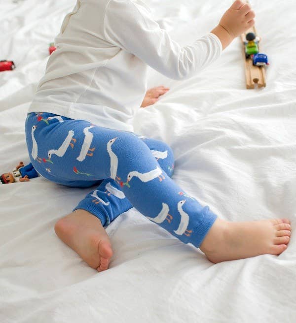 Child wearing blue leggings with animal pattern on a white bed