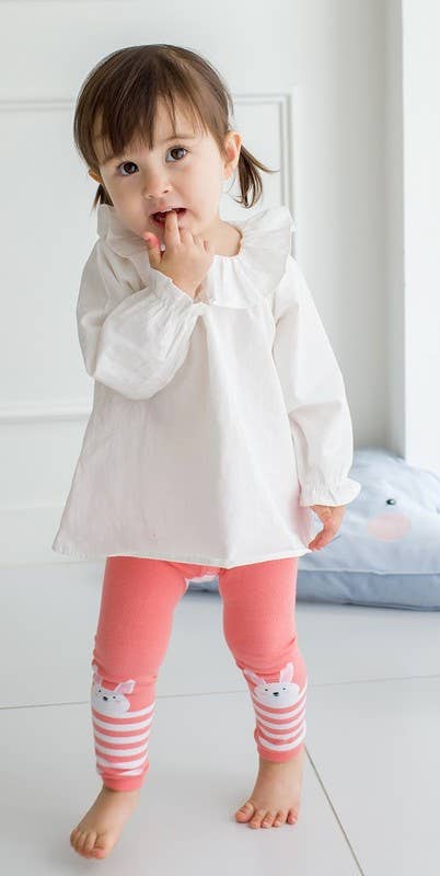 Child wearing a white shirt and pink striped leggings with animal designs.
