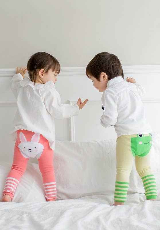 Two children wearing colorful leggings with animal prints on a white bed.