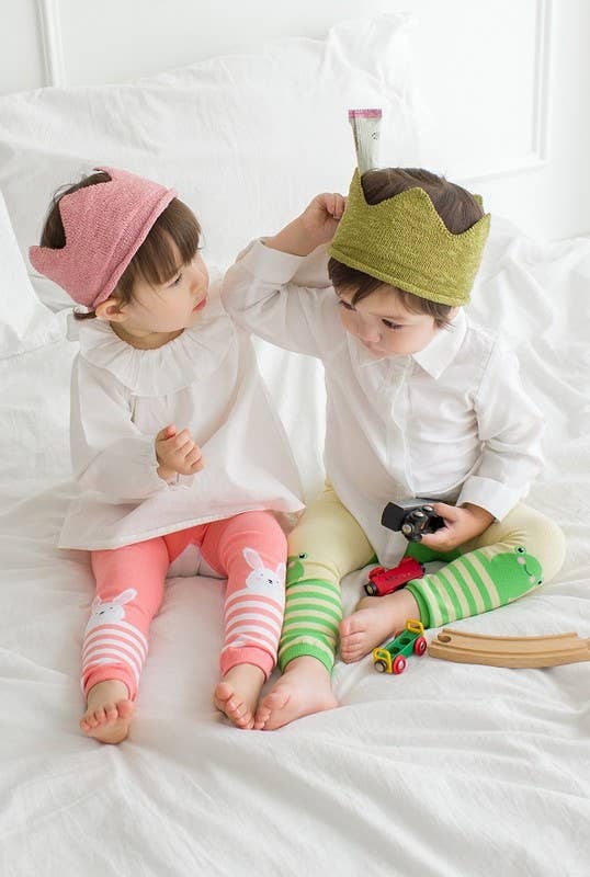 Two children wearing colorful hats and socks sitting on a bed.