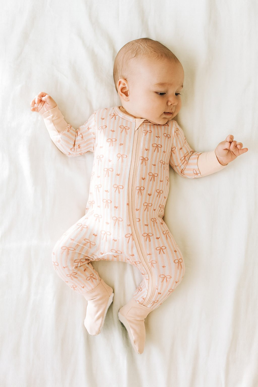 Baby wearing a patterned onesie lying on a white surface