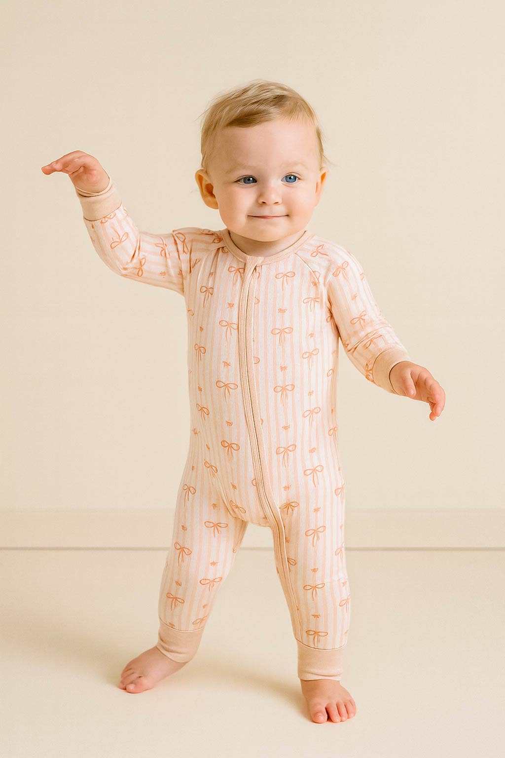 Baby wearing a light pink onesie with a subtle pattern on a beige background
