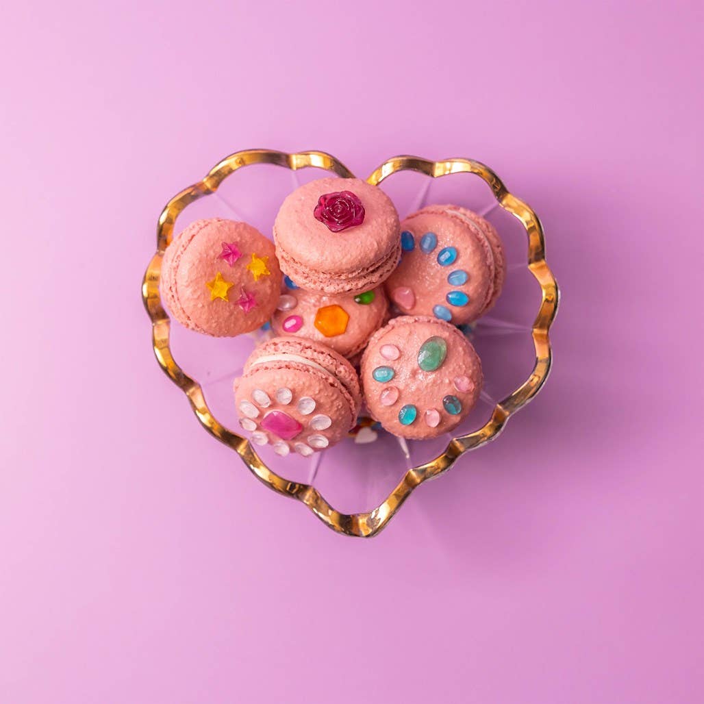 Decorative pink macarons with colorful decorations on a heart-shaped gold plate against a pink background