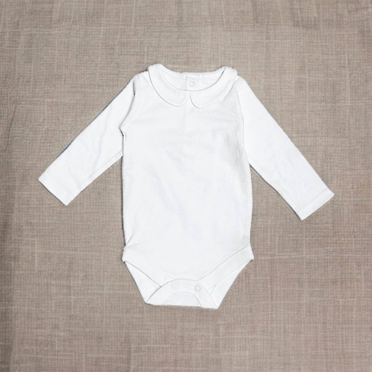 White baby onesie with long sleeves on a brown textured background