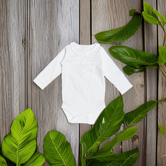 White baby onesie on a wooden surface with green leaves