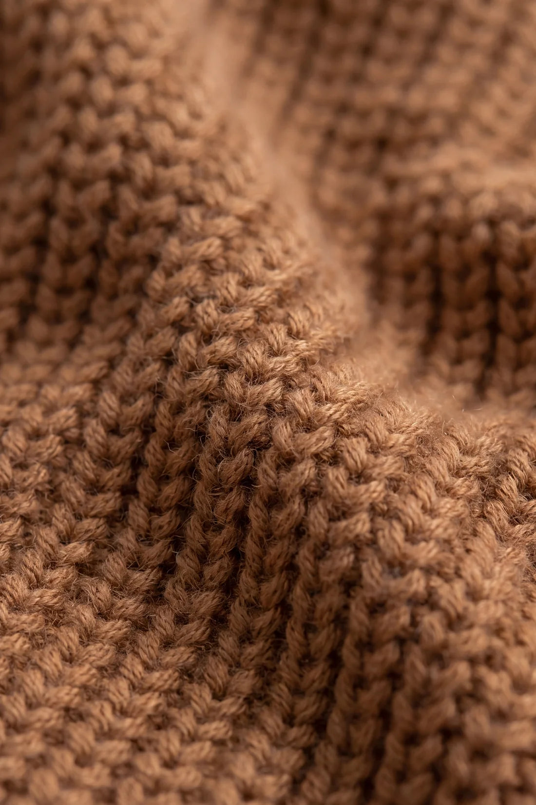Close-up of a brown ribbed knit fabric texture with soft folds and visible yarn details.