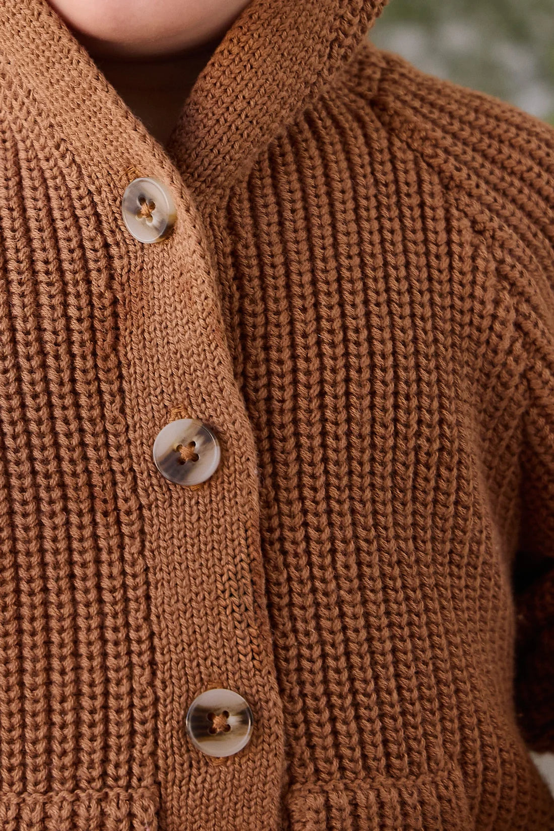 Close-up of a ribbed knit brown cardigan sweater with four brown buttons, worn by a person.